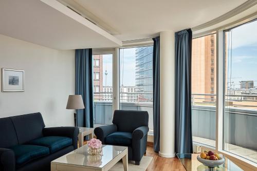 a living room with a couch and chairs and windows at The Mandala Berlin, a Member of Design Hotels in Berlin