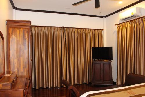 a bedroom with a bed and a tv and curtains at Lux Hotel in Luang Prabang