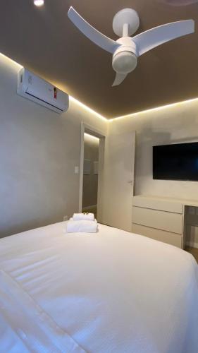 a bedroom with a white bed with a ceiling fan at Apart-hotel Theotókos Flats in Piumhi