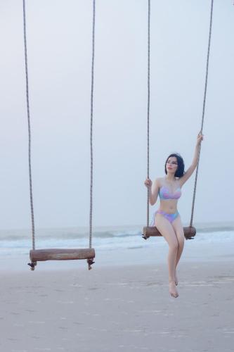a woman in a bikini sitting on a swing on the beach at Flamingo Hai Tien in Nam Khê