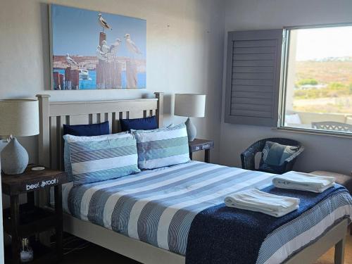 a bedroom with a bed with blue and white sheets and a window at MADRIKO 36 Cozy self catering 2 bedroom apartment in Langebaan
