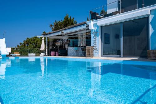 a swimming pool with blue water in front of a house at Ikaria Beachfront Villa 7 Bedrooms Villa Indigo Blue Haven Infinity Pool With Stunning Aegian Sea Views Gialiskari in Gialiskari