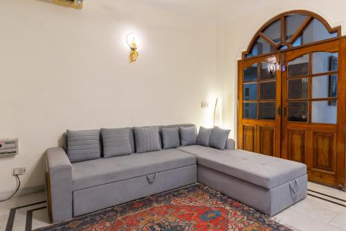 a living room with a gray couch in front of a door at Homlee-Green Luxury 3BHK-South DEL-NFC-Fortis Hospital in New Delhi