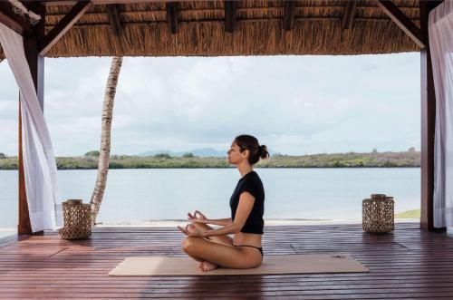 a woman sitting on a yoga mat in front of the water at One&Only Le Saint Géran, Mauritius in Belle Mare
