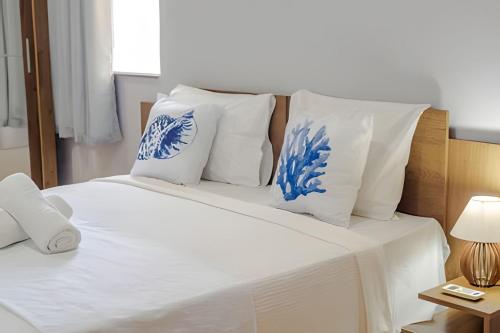 a bed with white sheets and blue and white pillows at 500m PRAIA de Taperapuan; 2 quartos; WiFi 300mbs; 2 pavimento; Churrasqueira; Chuveirão; Estacionamento Gratuito 1 carro in Porto Seguro