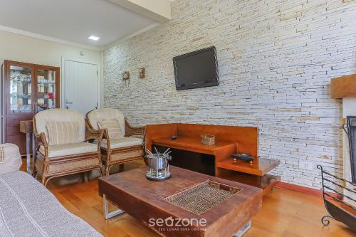 a living room with a couch and a tv on a brick wall at Apto c/ Linda Vista em Campos do Jordão LVR0003 in Campos do Jordão