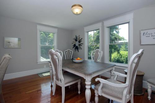 a dining room with a table and chairs and windows at Pocasset Village Charmer in Pocasset