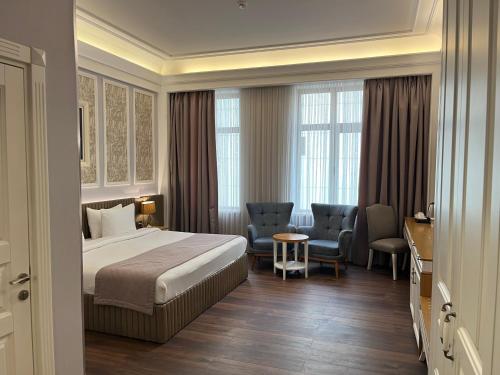 a hotel room with a bed and chairs and windows at Theatrum Hotel Baku in Baku