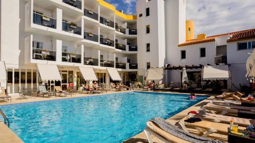 a swimming pool in front of a hotel with people sitting on chairs at Hotel do Cerro in Albufeira