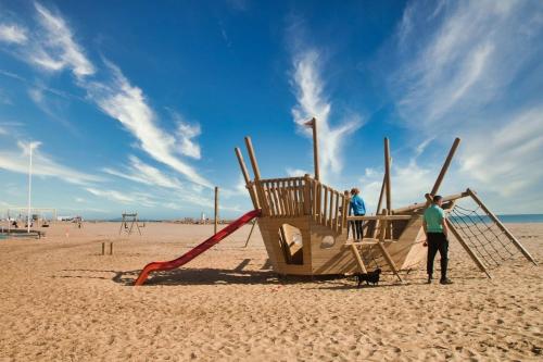 zwei Personen stehen neben einem Spielplatz am Strand in der Unterkunft Vos vacances à la mer in Valras-Plage