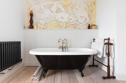 a bath tub in a bathroom with a painting on the wall at Painter's Cottage in the Cotswolds in Woodchester