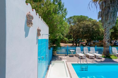 a swimming pool next to a white wall with a blue fence at Agriturismo Costa del Sud in Teulada