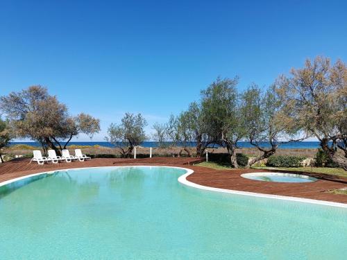 a swimming pool with two white chairs and trees at Spiaggiabella Resort in Torre Rinalda