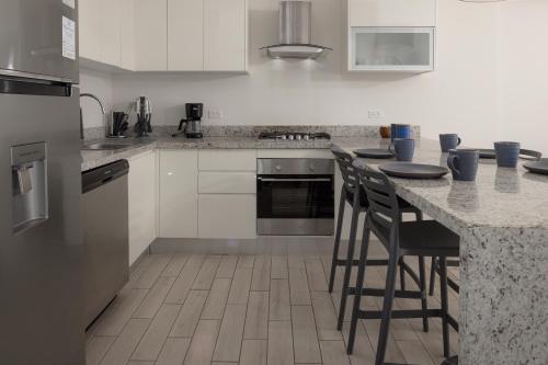 a kitchen with white cabinets and a counter with stools at Sanctuary by Playa Caracol Frente al Mar in Punta Chame