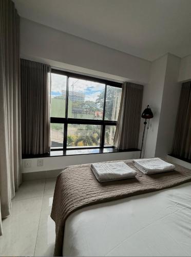 a bedroom with a bed and a large window at Studio Compacto com Design Clean no Vertigo in Campo Grande