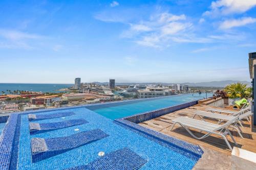 a pool on the roof of a building with chairs and the ocean at Monyxbnb at Zoho Skies in Puerto Vallarta