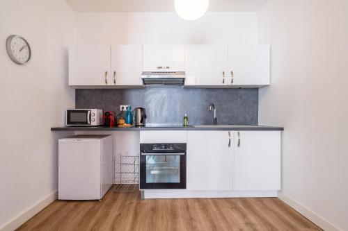 une cuisine blanche avec des placards blancs et une horloge dans l'établissement Hypercentre Capitole T2 vaste et lumineux, à Toulouse