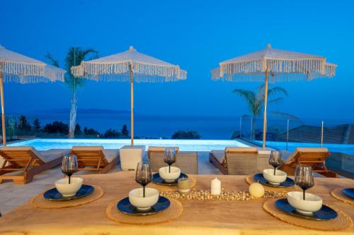 a dining table with chairs and umbrellas in front of a pool at Irena Stone Villas Kefalonia in Lourdhata