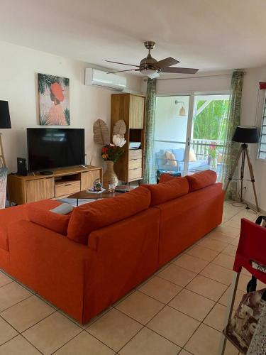 an orange couch in a living room with a flat screen tv at Residence piscine Ste Roses in Îlet à Christophe