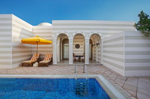 a swimming pool with chairs and an umbrella next to a house at The Oberoi Beach Resort, Sahl Hasheesh in Hurghada