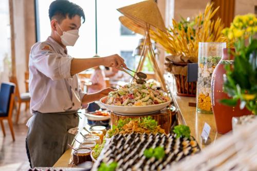 a man in a mask preparing a buffet of food at Sala Quy Nhon Beach Hotel in Quy Nhon