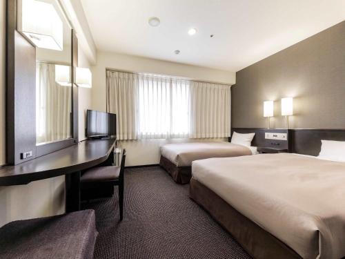 a hotel room with two beds and a desk at Nishitetsu Inn Kokura in Kitakyushu