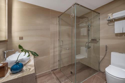 a glass shower stall in a bathroom with a toilet at Canvas Danang Beach Hotel in Da Nang