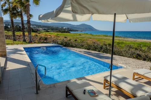 a swimming pool with an umbrella and chairs and a table and an umbrella at Kallisti Beach & Spa Villa - A Luxury Seaside Retreat in Lachi