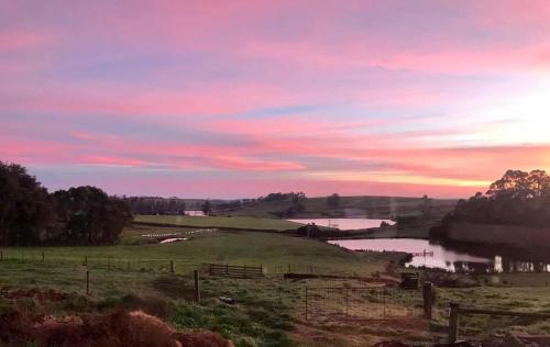 a sunset over a field with a lake and a fence at Robin Hoods Well Farm Stay in Sassafras