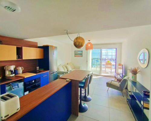 une cuisine avec des placards bleus et une table avec des chaises dans l'établissement LE MILLESIME OLIVIER : Vue exceptionnelle sur la baie, appartement moderne avec une chambre et parking privé., à Marseillan