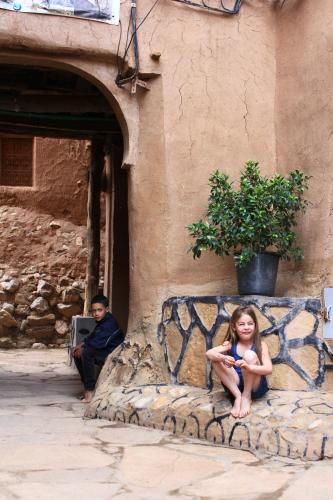 a young girl sitting on a bench next to a building at Kasbah Maison D’hôte Lalla Zahra in Aït Baha