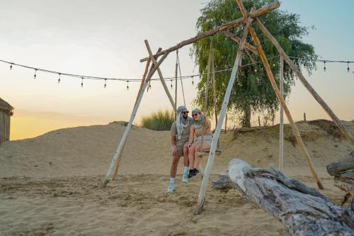 two people sitting on a swing in the sand at Al Marmoom Oasis Luxury Tents and Bedouin Experience in Dubai