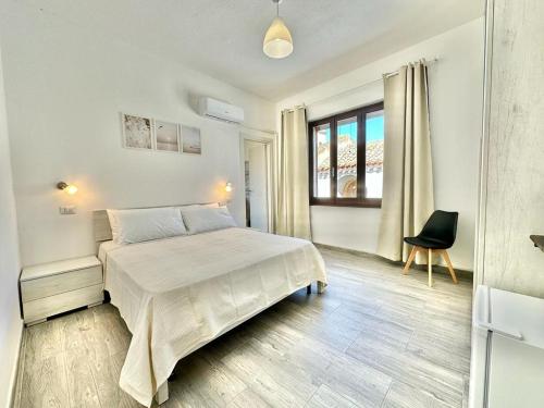 a white bedroom with a bed and a chair at Bonòra Suites in Tortolì