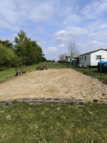 un chemin de terre dans un champ avec deux bancs dans l'établissement MOBIL-HOME 6 personnes St Vivien de Médoc 33, à Saint-Vivien-de-Médoc