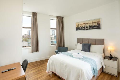 a bedroom with a bed and a desk and two windows at London City Hotel in Woolwich