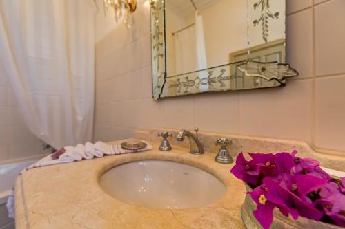 a bathroom with a sink with a mirror and purple flowers at IPEKYOL Guesthouse in Çeşme