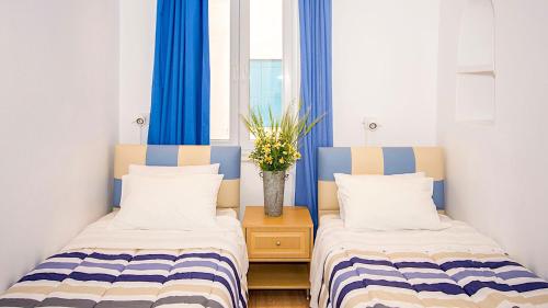 two beds in a small room with blue curtains at Pension Ageliki Kalogera in Mikonos