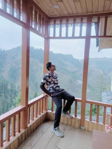 a man sitting on a balcony looking out at the mountains at Apple Land by Naavagat in Jibhi