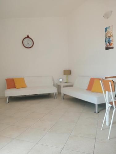 a living room with two white couches and a clock on the wall at Le Rondini in Sorso
