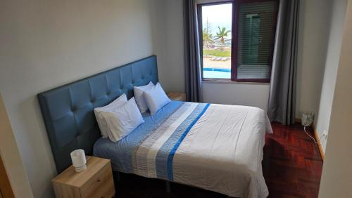 Un dormitorio con una cama con cabecero azul y una ventana. en CRISTO REI APARTMENT, en Caniço