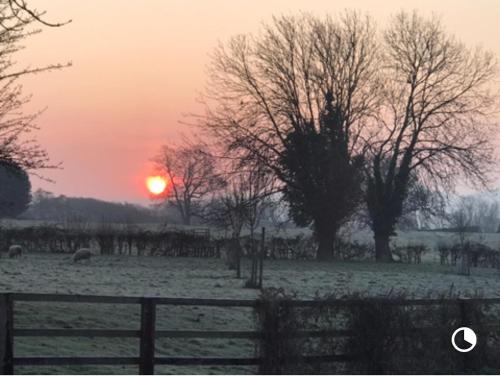 a sunset in a field with a fence and trees at Apartment above Samantha Dadd Art Studio - in the Cotswolds in Tewkesbury