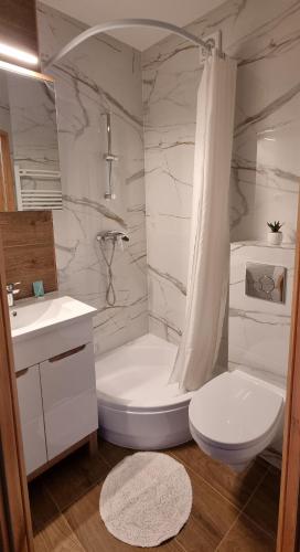 a white bathroom with a toilet and a tub and a sink at Pod Żaglami in Pobierowo