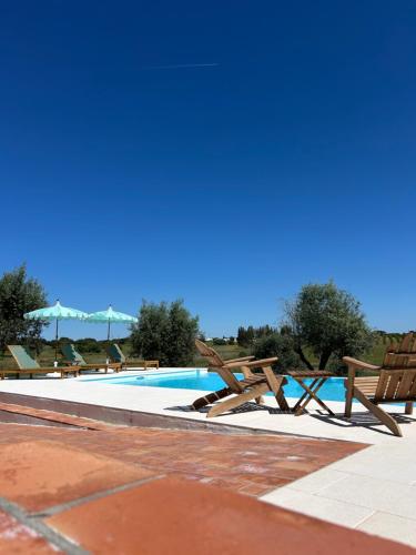 a swimming pool with wooden chairs next to it at DoVale Country House in Fronteira
