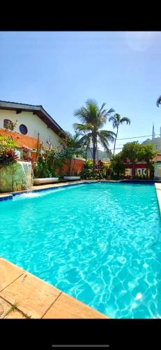 a large blue swimming pool with palm trees in the background at Pousada Dolce Vita in Itanhaém