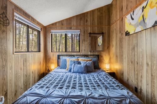 a bed in a room with wooden walls and windows at 2-bedroom cabin, with a Fireplace, PS5, BBQ, fitness room, and a private hot tub in Hedgesville