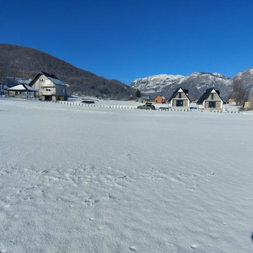 a snow covered field with houses and mountains in the background at BOK Holiday VILLAGE Kolasin in Kolašin