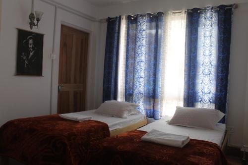 two beds in a room with blue curtains at Mansarover Home Stay in Kalimpong