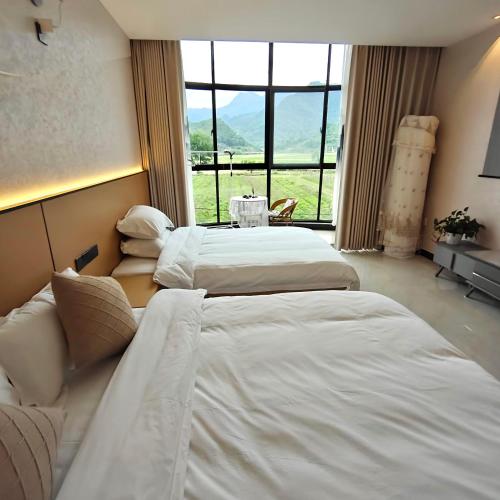 two beds in a hotel room with a large window at Wangxian Valley Qingchuanxingguan - Wangxian Valley Scenic Area in Jiangcun