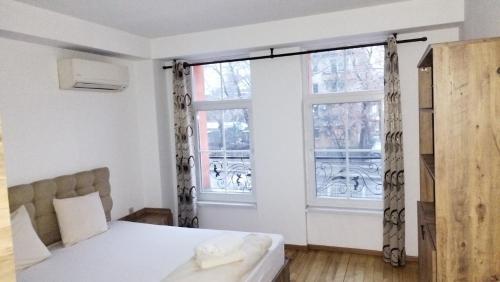 ein Schlafzimmer mit einem Bett und zwei Fenstern in der Unterkunft Center Apartments The Quiet Luxury 3 in Plowdiw