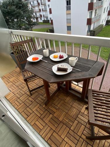 une table en bois avec deux assiettes de nourriture sur un balcon dans l'établissement Logement avec balcon, à Ouistreham